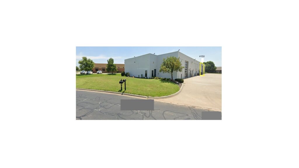 A small, white industrial building with a green lawn and clear skies.