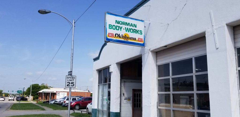 Exterior of Norman's Body Works auto repair shop with a visible sign and speed limit sign.