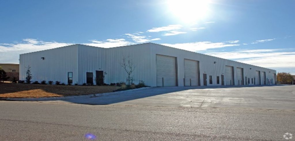 A large industrial warehouse with multiple garage doors under a bright sky.