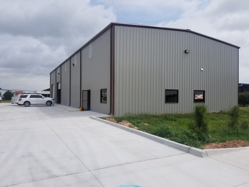 A metal industrial building with a concrete driveway and grassy area.