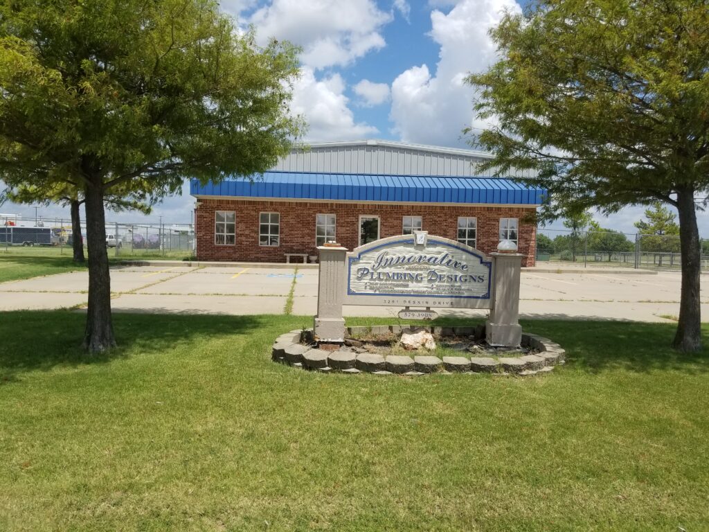 Entrance sign for a cemetery with a brick building in the background under a blue sky.