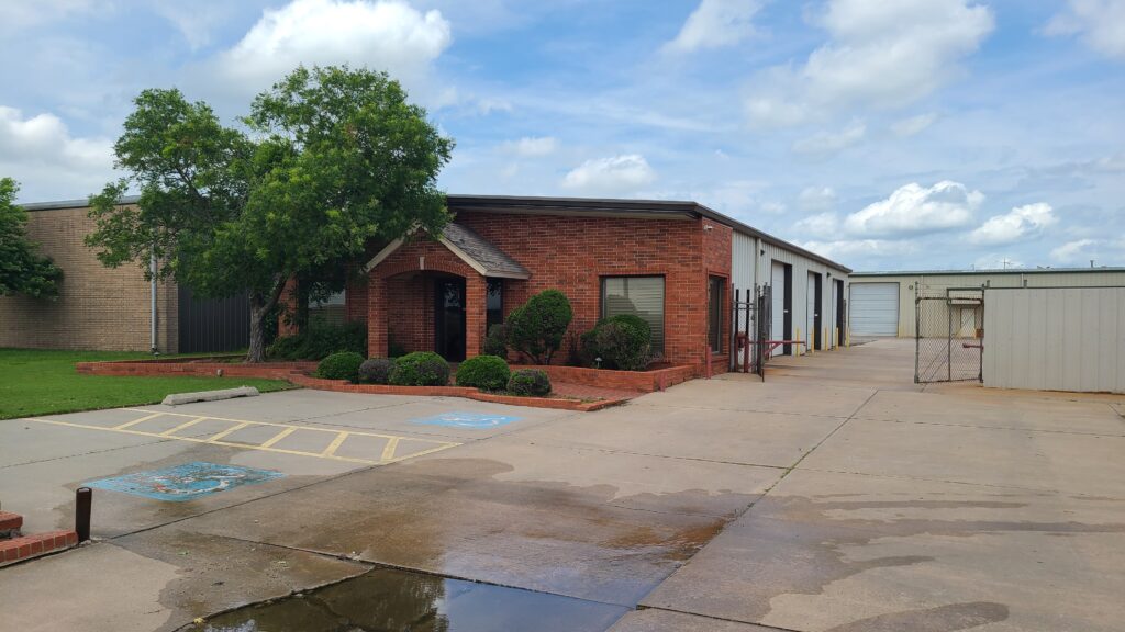 Brick commercial building with adjacent metal warehouse under a partly cloudy sky.