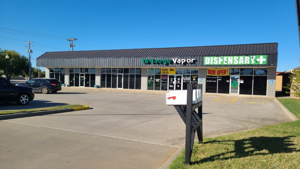 Strip mall with a vape store and dispensary under a clear blue sky.